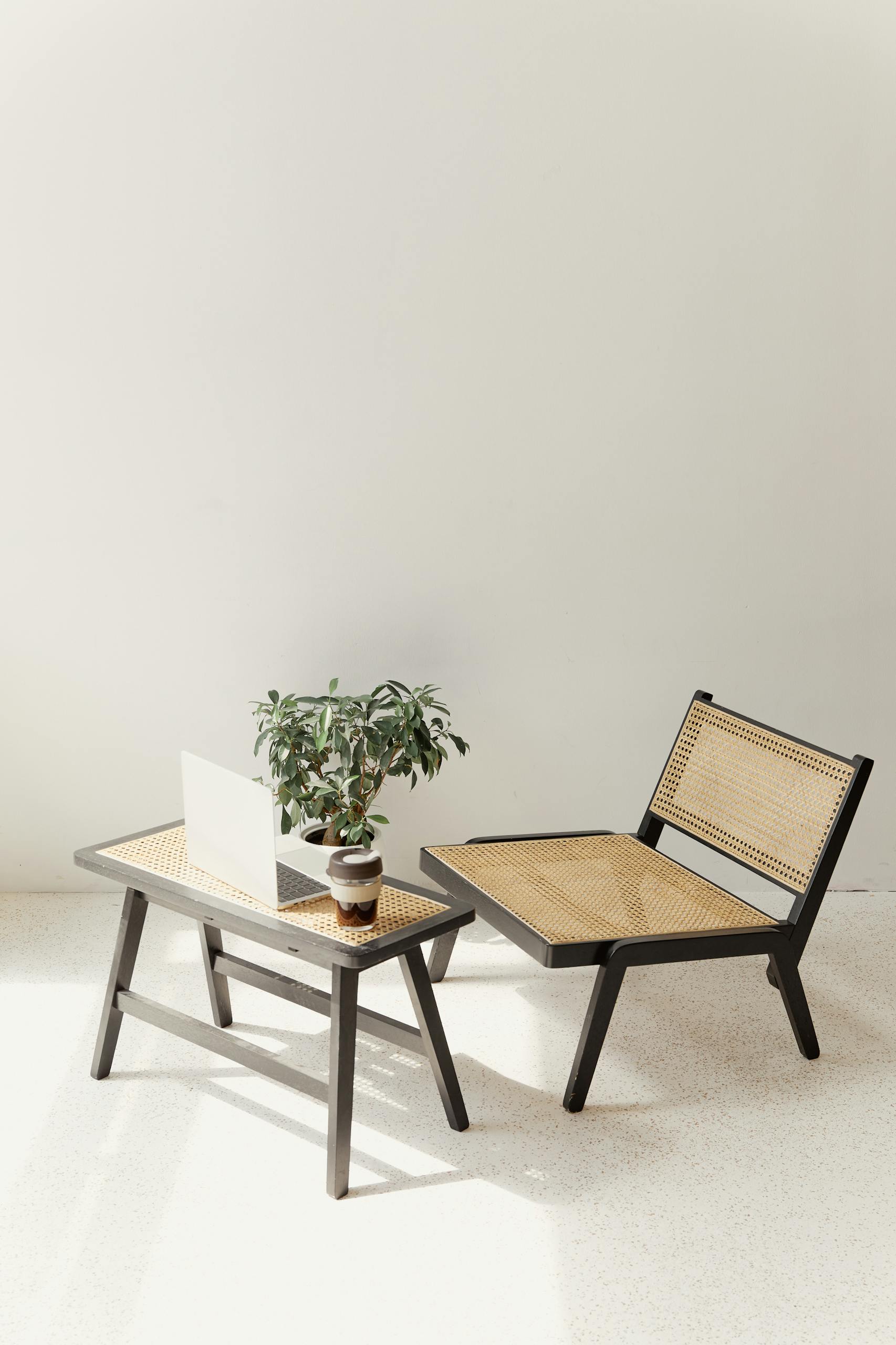 Stylish minimalist interior featuring a rattan chair, table, and laptop with a potted plant.